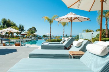 Limasol, Kıbrıs - 19 Mayıs 2021: Lüks modern otelin havuz alanı, palmiye ağaçları ve tropikal bitkilerin gölgesinde güneşli yataklar