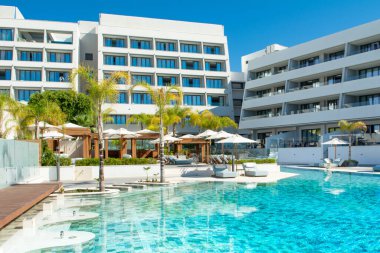 Limasol, Kıbrıs - 19 Mayıs 2021: Lüks modern otelin havuz alanı, palmiye ağaçları ve tropikal bitkilerin gölgesinde güneşli yataklar