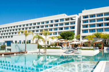 Limasol, Kıbrıs - 19 Mayıs 2021: Lüks modern otelin havuz alanı, palmiye ağaçları ve tropikal bitkilerin gölgesinde güneşli yataklar