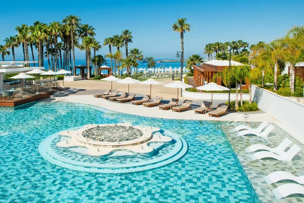 Limasol, Kıbrıs - 19 Mayıs 2021: Lüks modern otelin havuz alanı, palmiye ağaçları ve tropikal bitkilerin gölgesinde güneşli yataklar