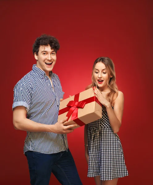 Chico le da a una chica un regalo en un estilo pin up, aislado en un bac rojo —  Fotos de Stock