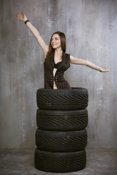 Young girl stands inside tires, spread his hands, on a backgroun — Stock Photo, Image