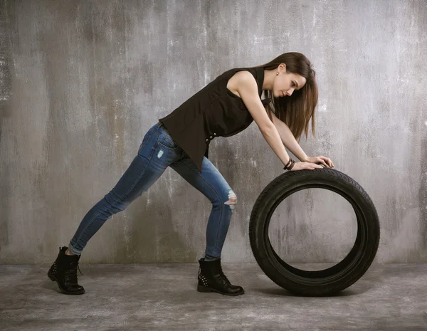 Fiatal, szexi lány wheels autó gumiabroncs, a háttérben a szürke konc — Stock Fotó