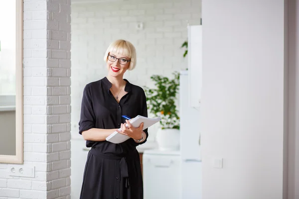 Mujer de negocios sonriente en un vestido negro con una revista para reco — Foto de Stock