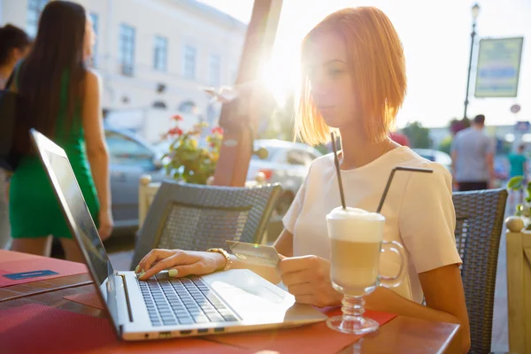 Chica con un ordenador portátil en un café, tienda con una tarjeta de crédito — Foto de Stock