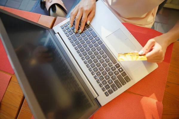 Chica con un ordenador portátil en un café, tienda con una tarjeta de crédito — Foto de Stock