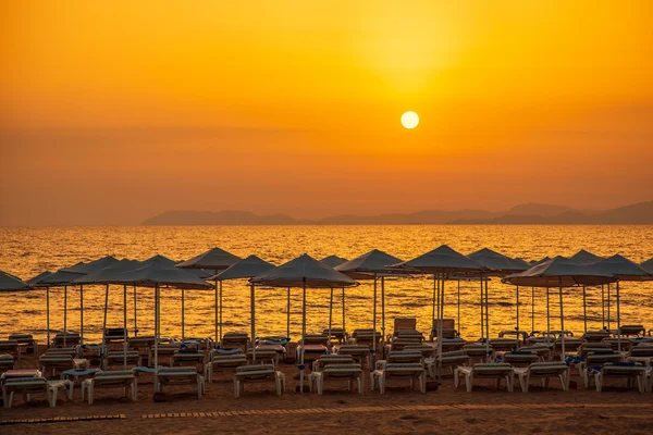 Puesta de sol en la playa de mar con tumbonas y sombrillas —  Fotos de Stock