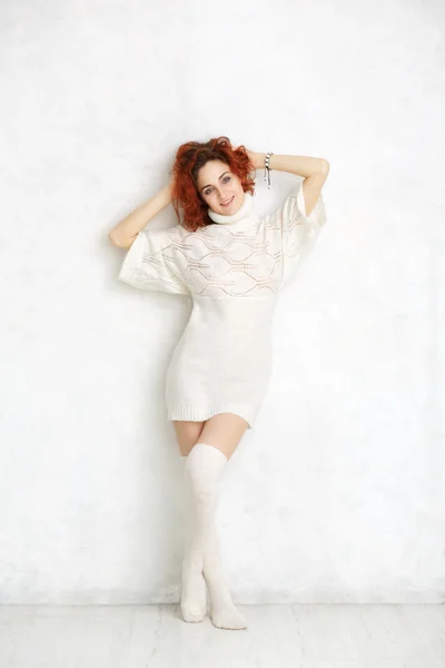 Redhead curly girl in a white knitted sweater and stockings stan Royalty Free Stock Images