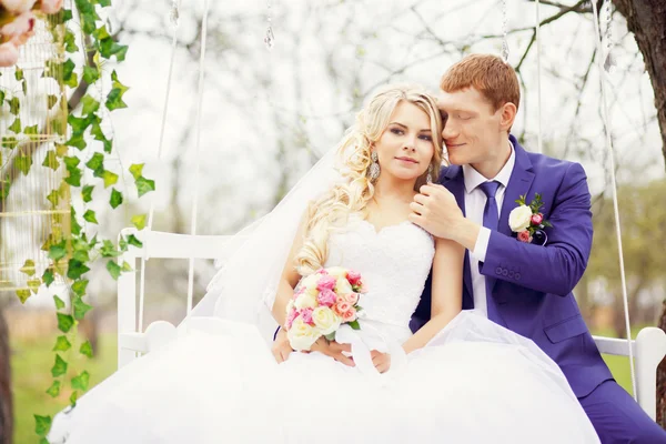 Young and beautiful bride and groom sitting on a white swing in — Stock Photo, Image