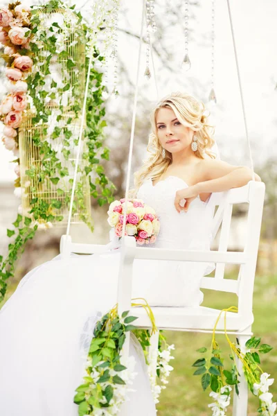 Young and beautiful bride sitting on a white swing in a spring g — Stock Photo, Image