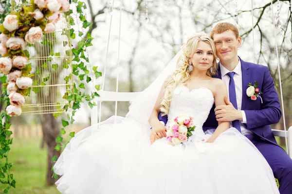 Young and beautiful bride and groom sitting on a white swing in — Stock Photo, Image