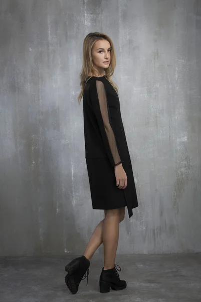 Fashionable girl in black dress standing on a gray background, t — Stock Photo, Image