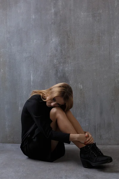 회색 콘크리트의 배경에 앉아 검은 드레스, 여자 — 스톡 사진