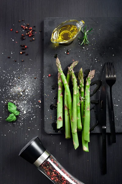 Asparagi freschi con olio d'oliva e condimenti su fondo scuro — Foto Stock