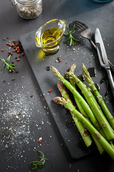 Frischer Spargel mit Olivenöl und Gewürzen auf dunklem Hintergrund — Stockfoto