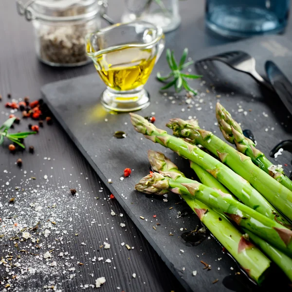 Fresh asparagus with olive oil and seasonings on dark background — Stock Photo, Image