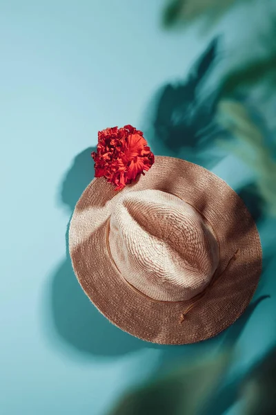 Sombrero de paja con flor tropical en azul con sombras de hojas de palma, plano — Foto de Stock