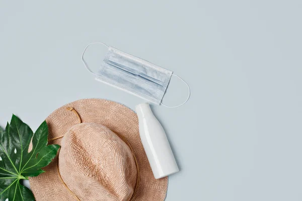 Strandzubehör: Strohhut, Sonnencreme und FFP2-Gesichtsmaske, isoliert auf Grau, Flatlay Stockbild