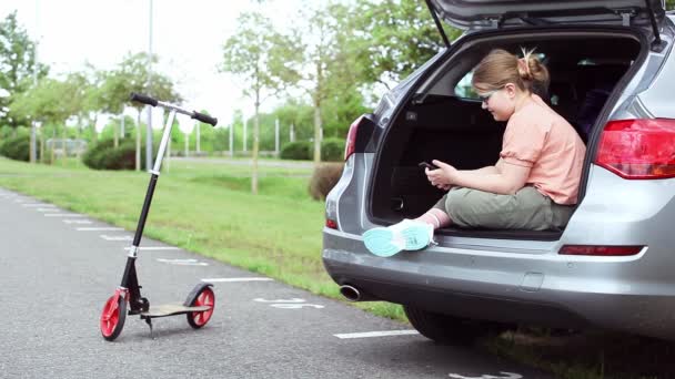 可爱的少女坐在车里，用智能手机无视她的摩托车和其他背景的孩子。使用技术概念的儿童. — 图库视频影像