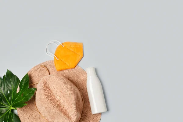 Beach accessories: straw hat, sunscreen lotion, exotic leaves and FFP2 face mask, isolated on grey, flatlay Stockfoto