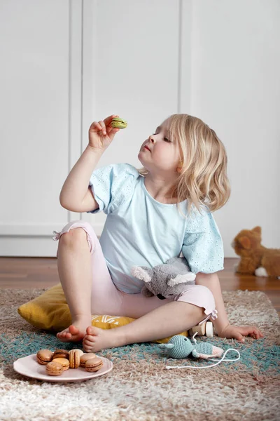 Little girl eating macarons on living room floor, natural light and airy indoor shot Stock Kép