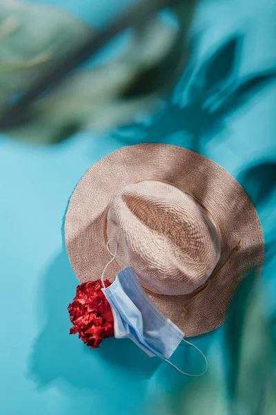 Sombrero de paja con flor tropical en azul con sombras de hojas de palma, plano Fotos de stock libres de derechos