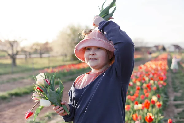Joven niña preadolescente recogiendo tulipanes en el campo, ella es feliz y sonriente, puesta de sol escena al aire libre. — Foto de Stock