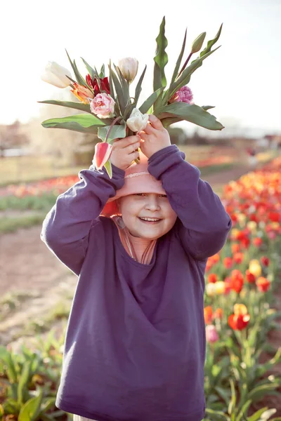 Jong tiener meisje stretching bos van tulpen naar de camera, zonsondergang outdoor scene. — Stockfoto