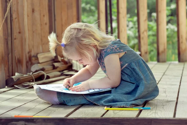 Menina desenho com lápis coloridos em uma casa de campo de madeira — Fotografia de Stock