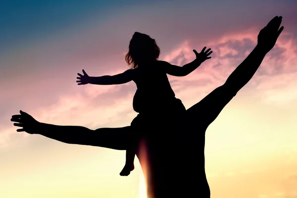 Силуэты счастливого отца и дочери против закатного неба — стоковое фото