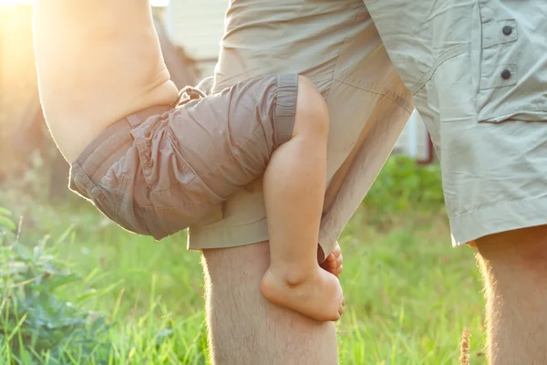 Little kid playing with his father and holding on to his legs — Stock Photo, Image