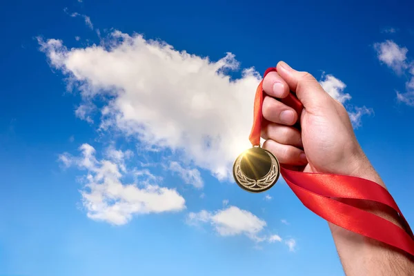 金メダルと赤いリボンで勝利を主張します メダルを手に 背景に雲と空 ストック写真