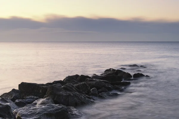 Stunning sunrise landscape over rocks in sea — Stock Photo, Image