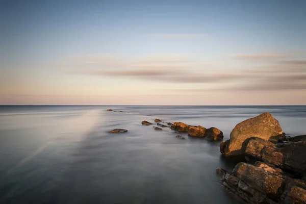 Atemberaubende Langzeitbelichtungslandschaft des Meeres über Felsen bei Sonnenuntergang — Stockfoto