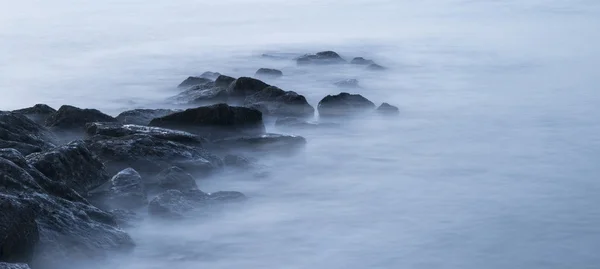 Peaceful cross processed landscape image of calm sea over rocks — Stock Photo, Image