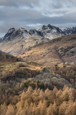 Epic Winter landscape image view from Holme Fell in Lake District towards snow capped mountain ranges in distance in glorious evening light clipart