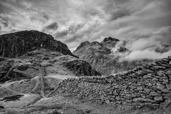 Stunning Winter  black and white landscape image of view from Side Pike towards Langdale pikes with low level clouds on mountain tops and moody mist