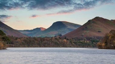 Derwent Water 'ın Güz Sonbaharı Gündoğumu sırasında yumuşak pastel renklerle göldeki güzel uzun pozlama manzarası.