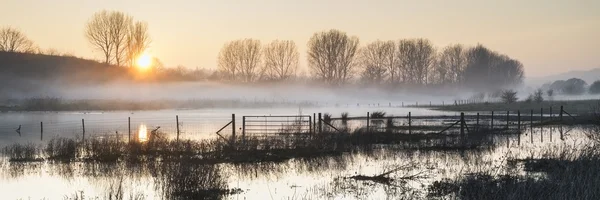 Panorama landschap van lake in mist met zon gloeien bij zonsopgang — Stockfoto