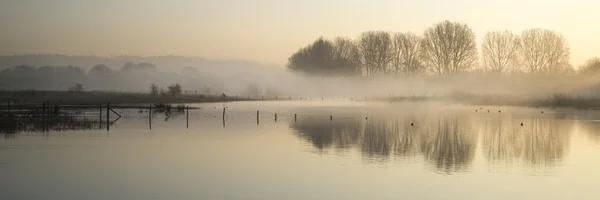 Panorama landschap van lake in mist met zon gloeien bij zonsopgang — Stockfoto