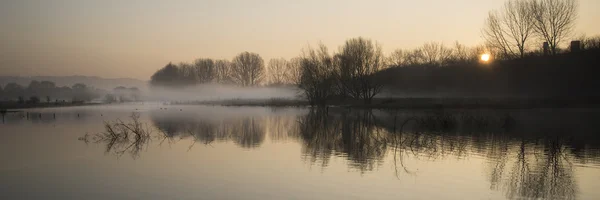 Panorama landschap van lake in mist met zon gloeien bij zonsopgang — Stockfoto