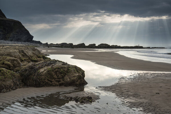 Stunning sun rays bursting from sky over empty yellow sand beach