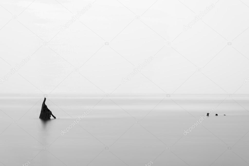 Minimalist landscape image of shipwreck ruin in sea black and wh