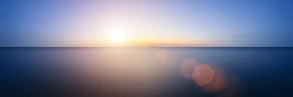 Imagen conceptual de la puesta del sol con destello de lente añadido sobre wate todavía — Foto de Stock