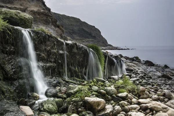 Landscape image of wide waterfall flowing onto rocky beach at su — Stock Photo, Image