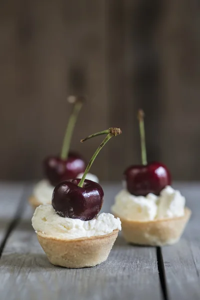 Cherry tartlets on rustic kitchen wooden background — Stock Photo, Image