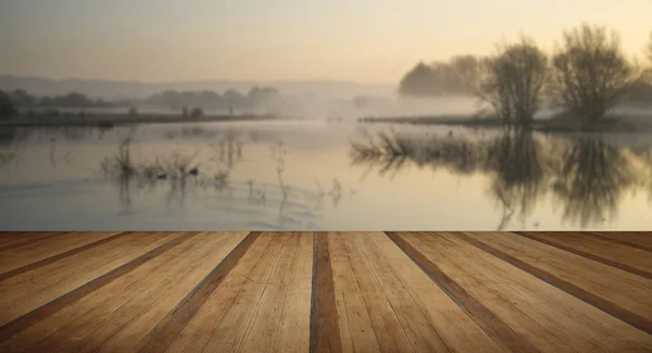 Paisaje de lago en niebla con sol resplandor al amanecer con madera p — Foto de Stock