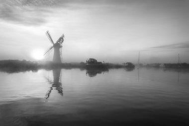 Stunnnig landscape of windmill and river at dawn in black and wh clipart