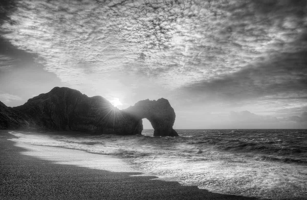 Zářivé slunce nad oceánem s rock zásobníku v popředí v blac — Stock fotografie