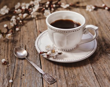 Чашка кофе на блюдце с ветками цветущей вишни на деревянной поверхности